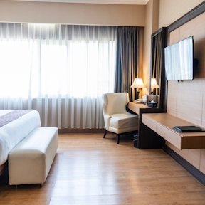 Sala de hotel luminosa con sofá blanco, sillón moderno y escritorio de madera junto a una ventana grande